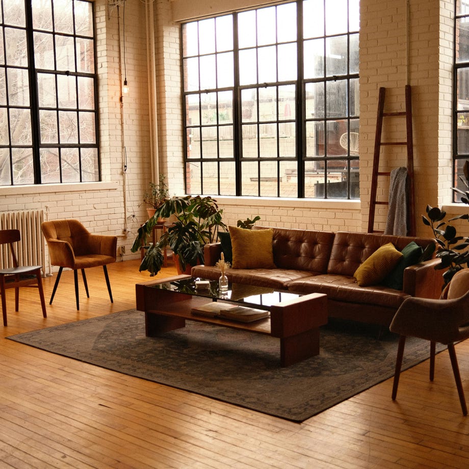 Spacious loft-style living room with modern furniture, large windows, and warm lighting.
